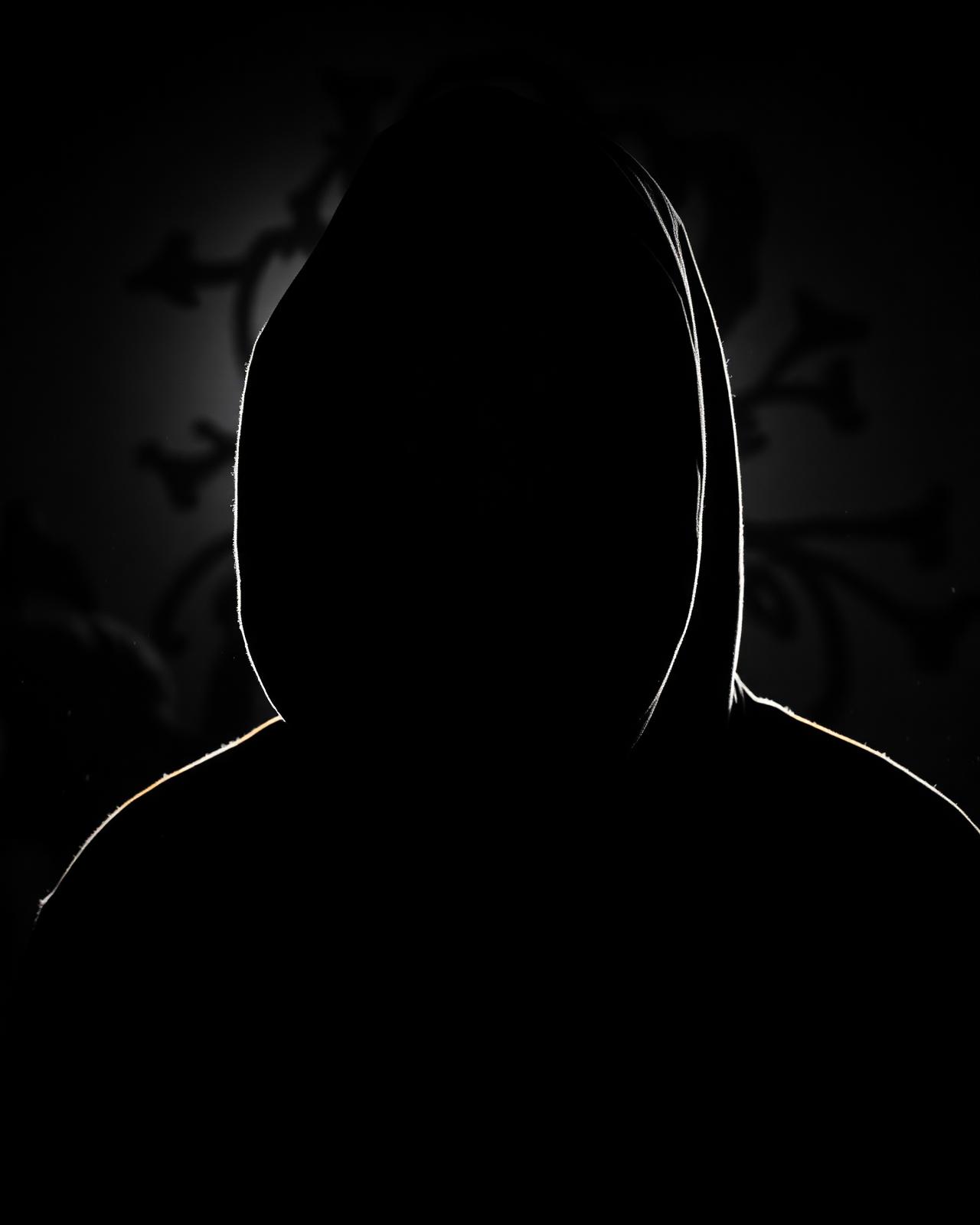Hooded silhouette rim-lit against a dark embellished background